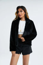 Woman wearing a black faux fur cropped jacket over a white top and black denim shorts, looking to the side.