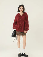 Full body shot of a woman in a red hooded cable knit cardigan and plaid skirt