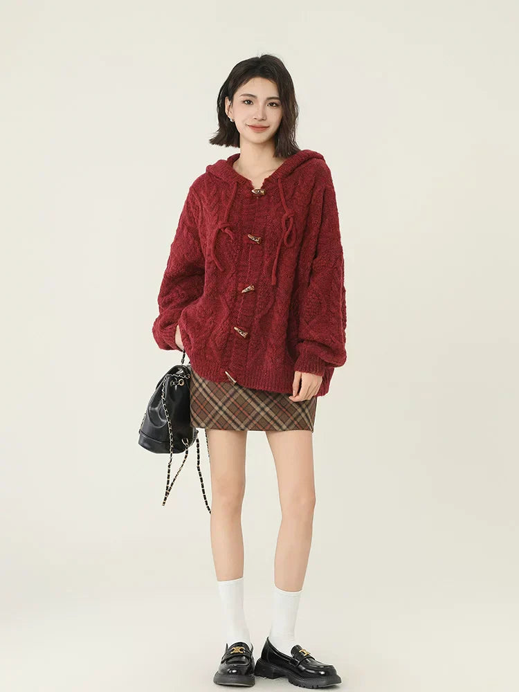 Full body shot of a woman in a red hooded cable knit cardigan and plaid skirt