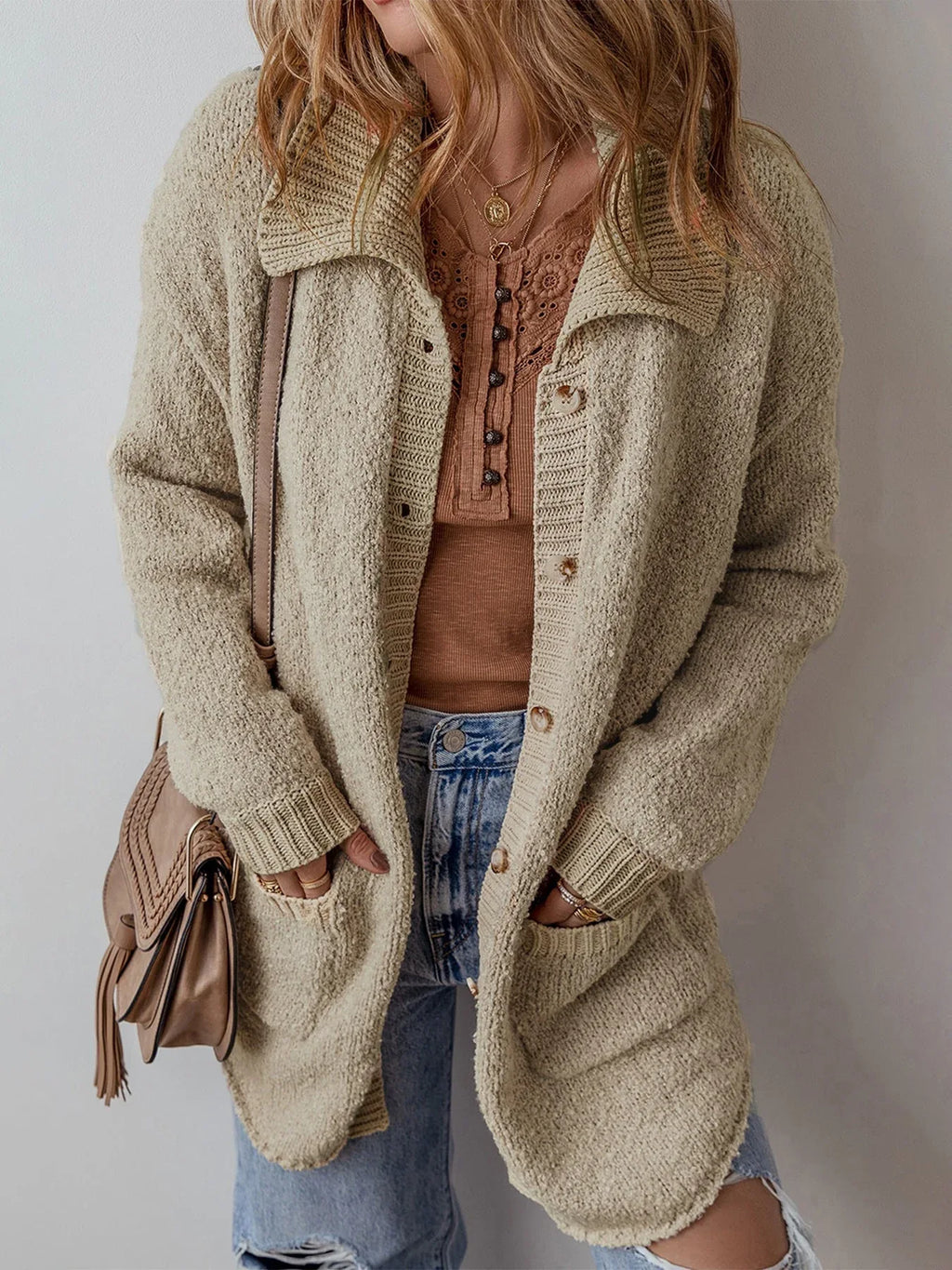 Front view of a woman wearing a beige textured knit cardigan over a brown top and blue jeans.