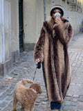 Woman wearing a long, striped faux fur coat and a knit hat, walking a dog.