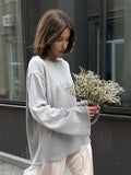 Woman wearing a light grey oversized knit sweater with bell sleeves