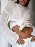 Woman tying the front of her white sheer knit sweater, revealing her midriff.