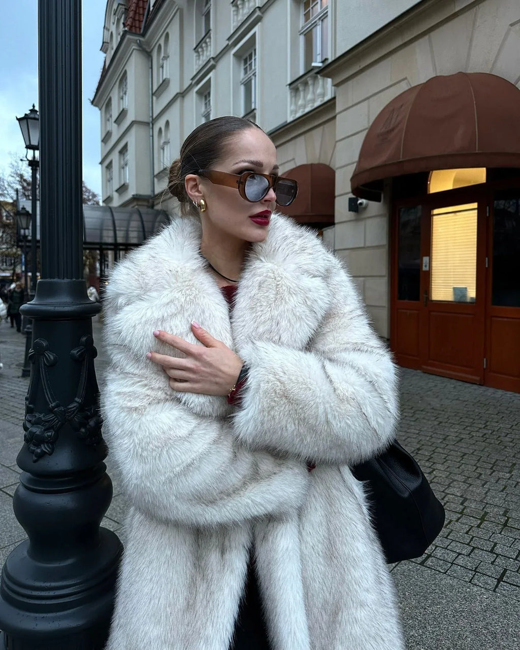 Woman wearing a white faux fur coat with wide lapels and full sleeves, standing outdoors.