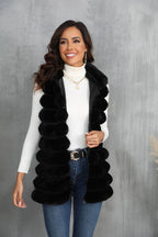 Woman wearing a black faux fur vest with a white turtleneck and blue jeans