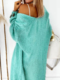 Woman from behind wearing a teal chunky knit cardigan draped off the shoulder, revealing a white tank top.