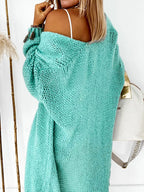 Woman from behind wearing a teal chunky knit cardigan draped off the shoulder, revealing a white tank top.
