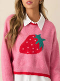 Close-up of a woman wearing a pink cropped knit sweater with a strawberry graphic, layered over a white collared shirt.