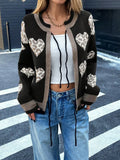 Woman wearing a black knit cardigan with a heart print and tie closure, layered over a white tank top.