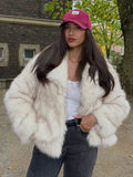 Fashionable woman wearing a cream faux fur jacket, dark jeans, and a pink baseball cap, looking at the camera.