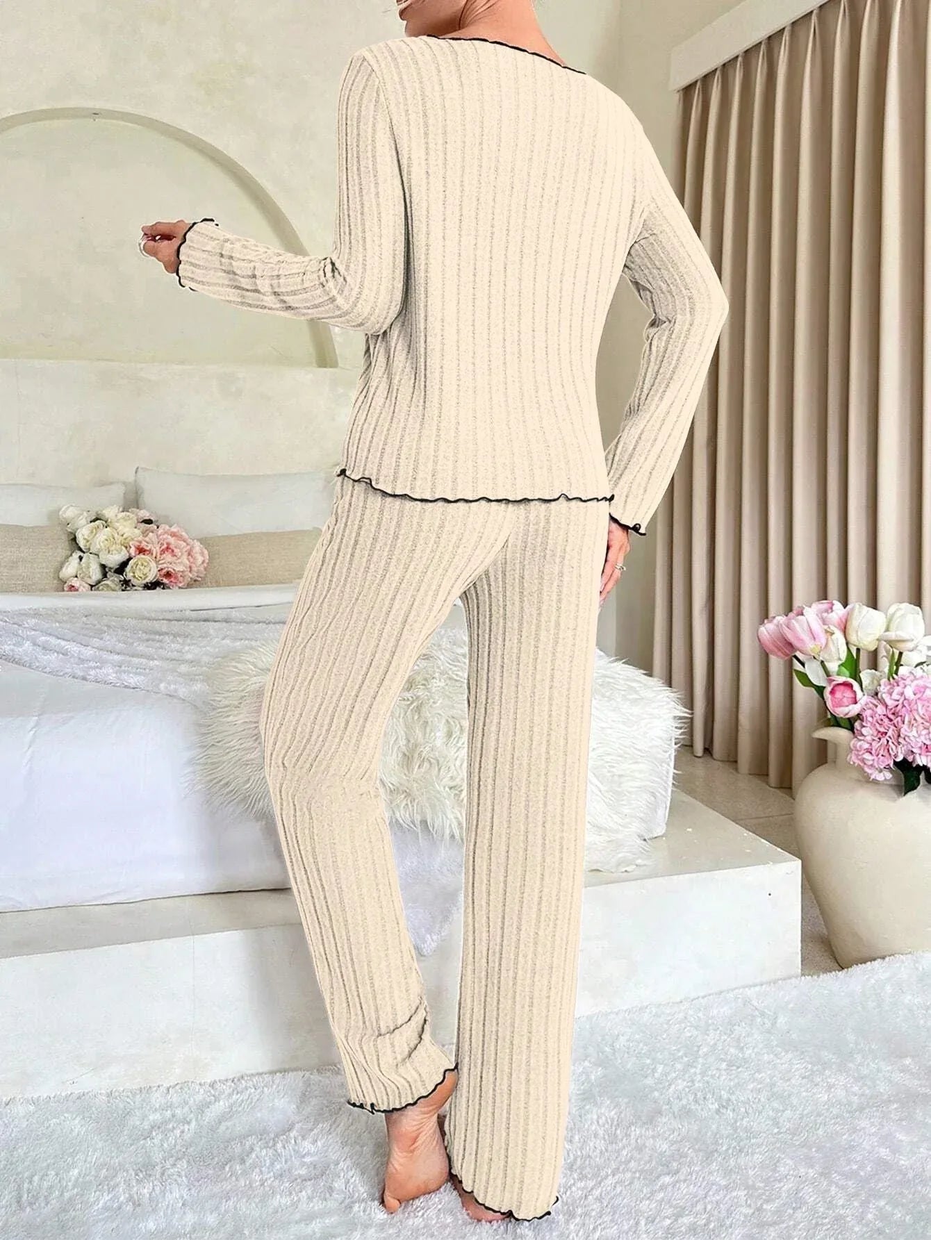 Back view of a woman in a cream-colored ribbed knit loungewear set with black trim and a black bow.
