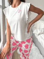 Close-up of a woman wearing a white top with ruffled sleeves and pink heart print pajamas