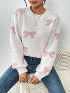 Woman wearing a white knit sweater with a pink bow print and crew neckline.