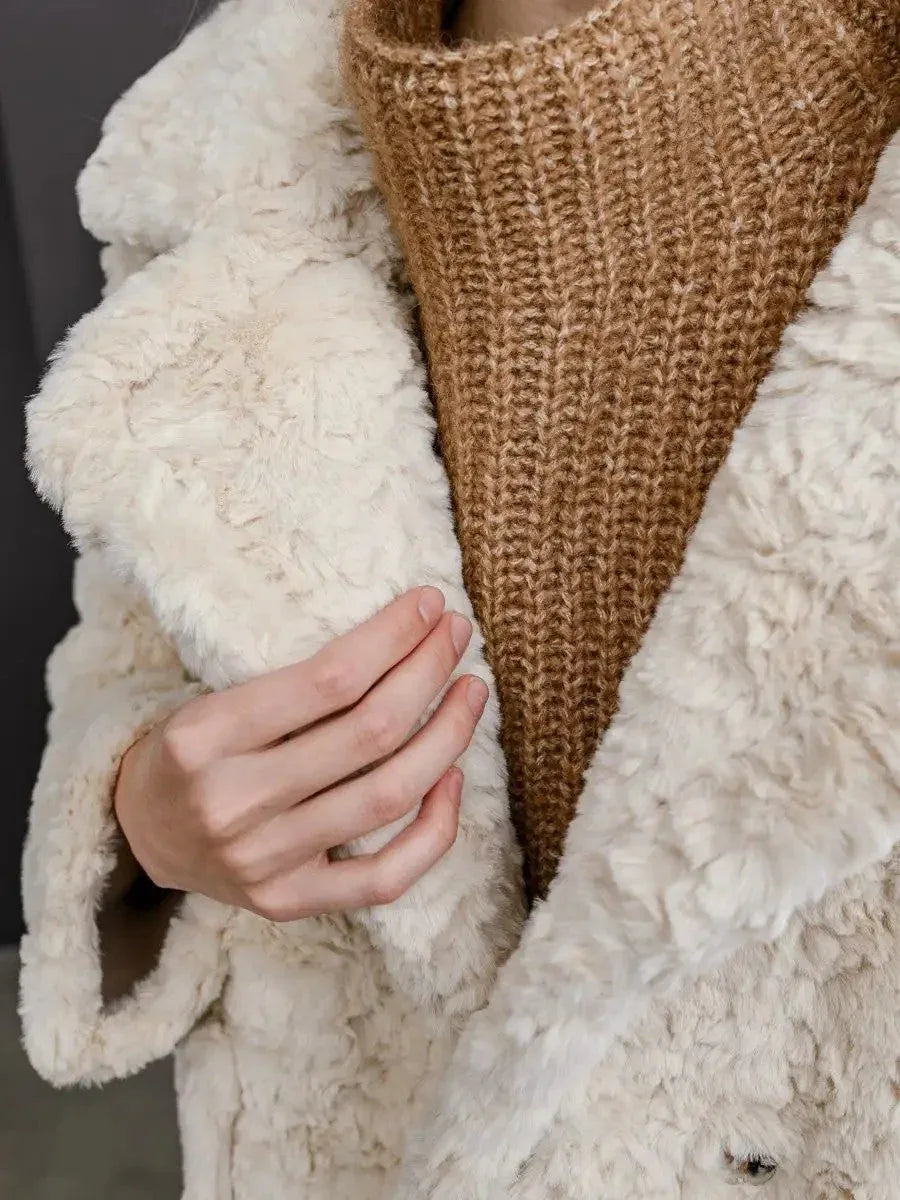 Close-up of the cream faux fur coat showing texture and the brown knit sweater underneath.