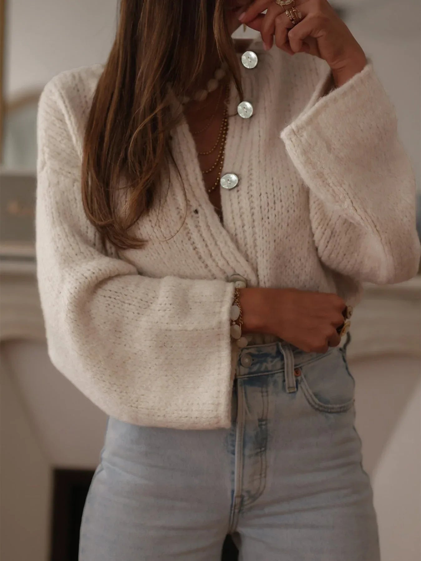 Woman in a cream knit cardigan and light wash denim jeans.