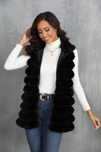 Woman smiling and touching her hair while wearing a black faux fur vest