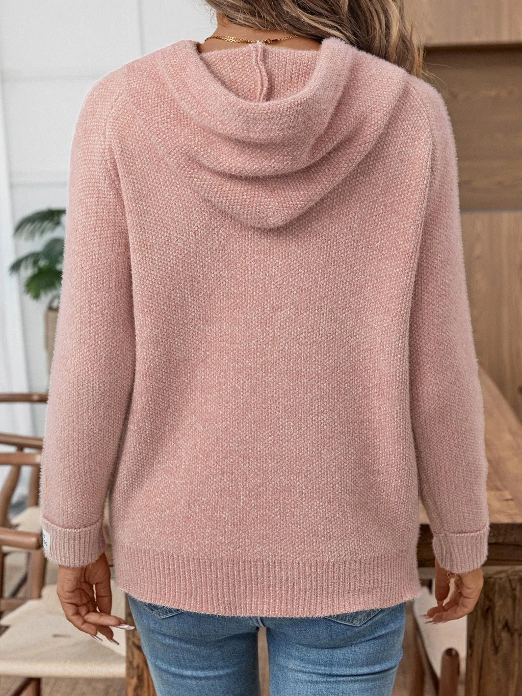 Woman wearing a pink hooded knit sweater with blue denim jeans, back view
