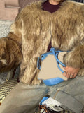 Detail of a woman's brown faux fur jacket and a blue handbag