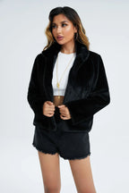 Woman wearing a black faux fur cropped jacket over a white top and black denim shorts, holding the front of the jacket.