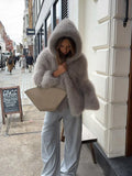 Woman in a grey hooded faux fur jacket and light blue pants holding a handbag