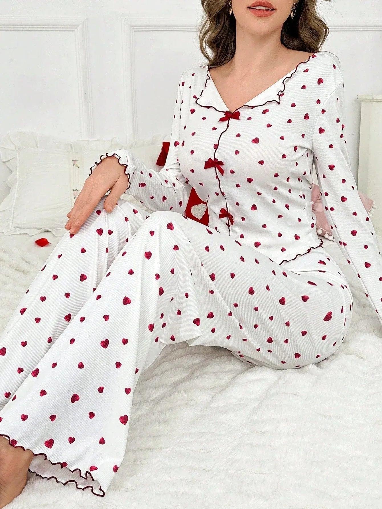 Woman sitting on a couch wearing a white long-sleeve pajama set with a red heart print and red trim.