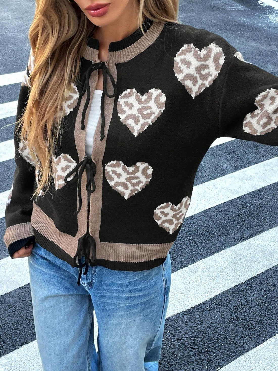 Woman wearing a black knit cardigan with a heart and leopard print pattern, featuring a tie closure and contrast trim.