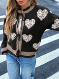 Close-up of a woman in a black knit cardigan with a heart and leopard print, showing the tie detail.