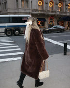 Woman walking on a street wearing a long brown faux fur coat