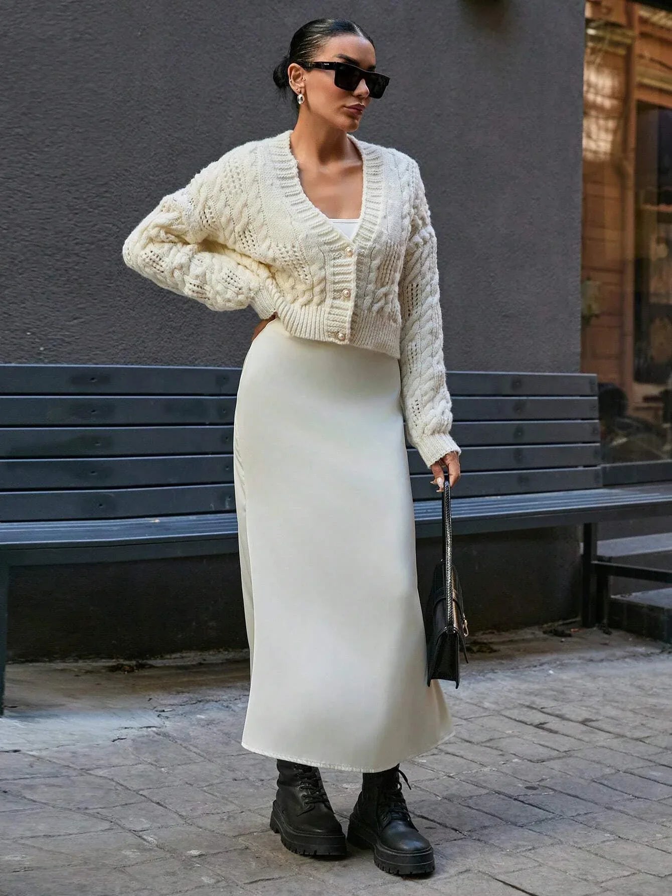 Woman wearing a cream cable knit cropped cardigan with pearl buttons and a matching cream slip skirt.