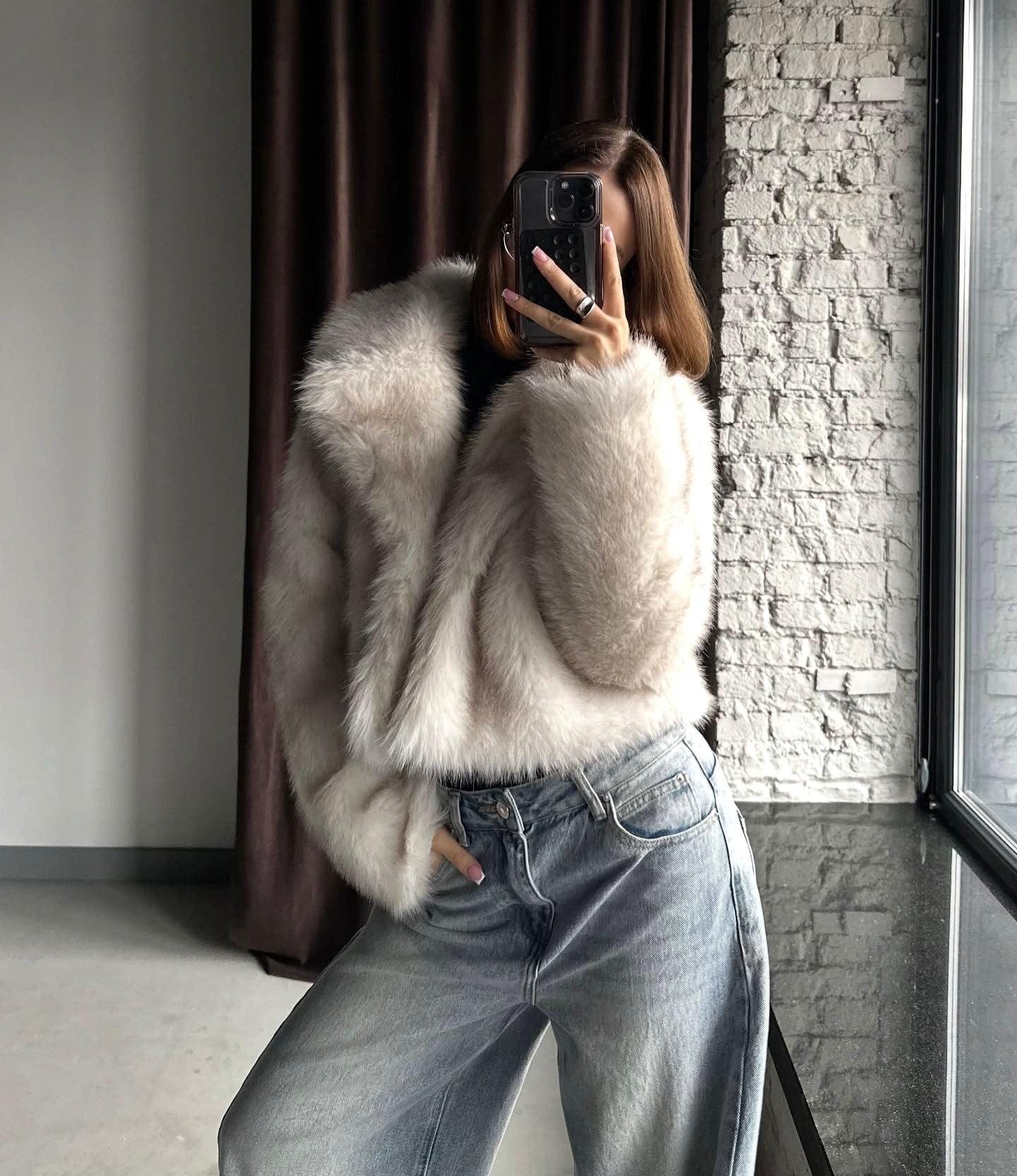 Front view of a woman in a cream faux fur jacket and light wash wide-leg jeans.
