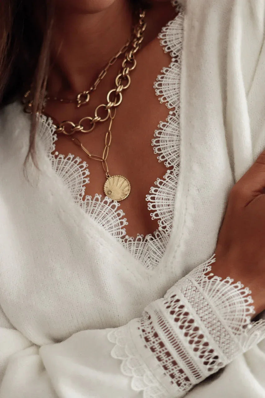 Detailed view of the lace trim on the V-neckline and cuffs of a white knit sweater.