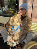 Woman sitting outdoors in a brown faux fur jacket and grey pants