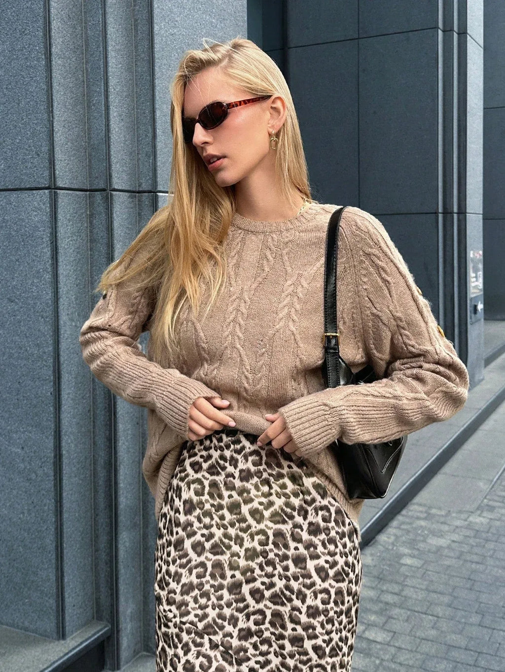 Back view of a woman wearing a tan textured knit sweater with long sleeves and a curved hem, paired with blue jeans.
