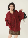 Woman holding a black bag while wearing a red hooded cable knit cardigan