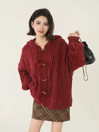 Woman holding a black bag while wearing a red hooded cable knit cardigan