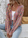 Woman sitting down wearing a rainbow multicolor open-knit cropped cardigan with a v-neck and button-front closure, styled with a white top and blue jeans.