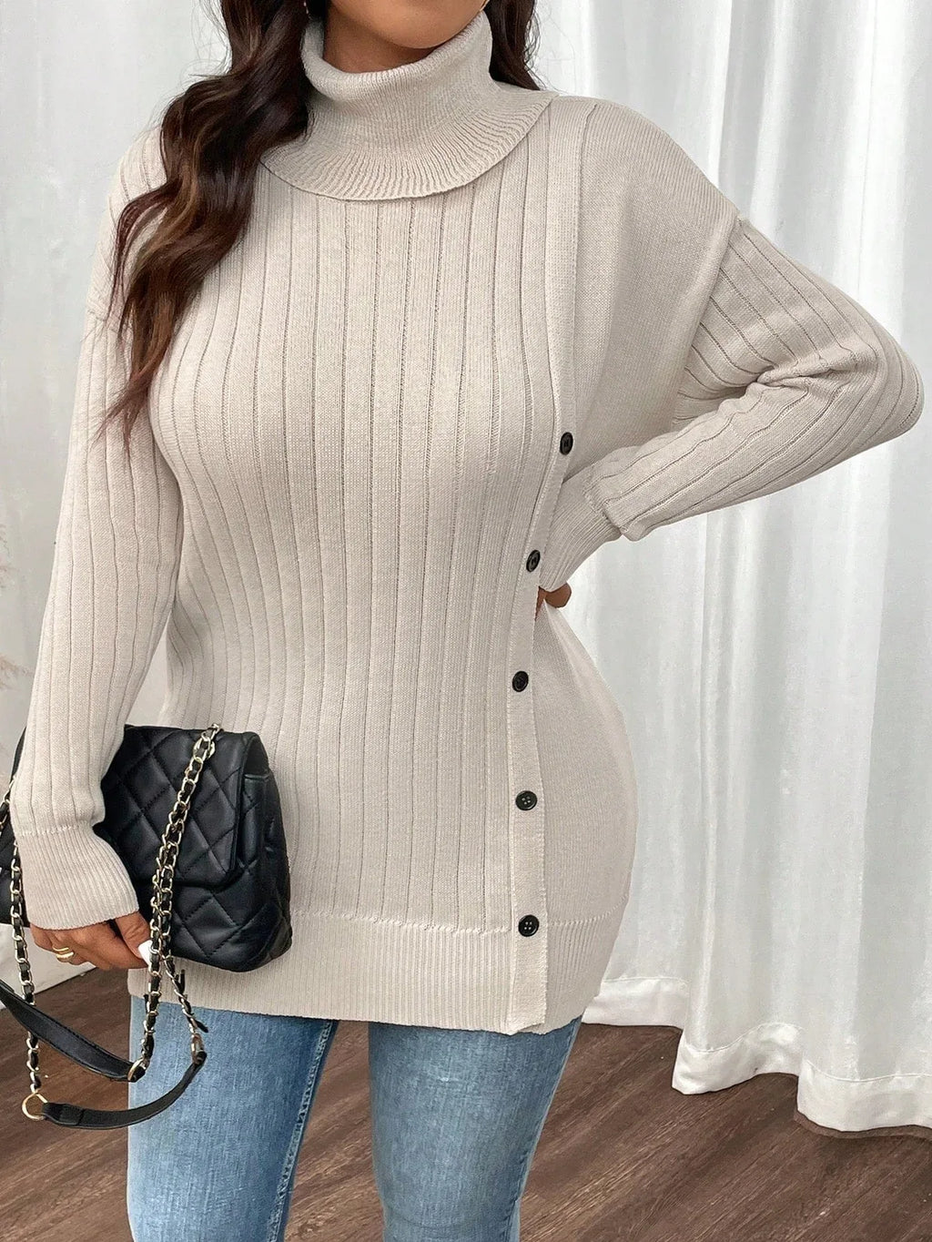 Close-up of a woman wearing a cream ribbed knit turtleneck tunic sweater with side buttons.