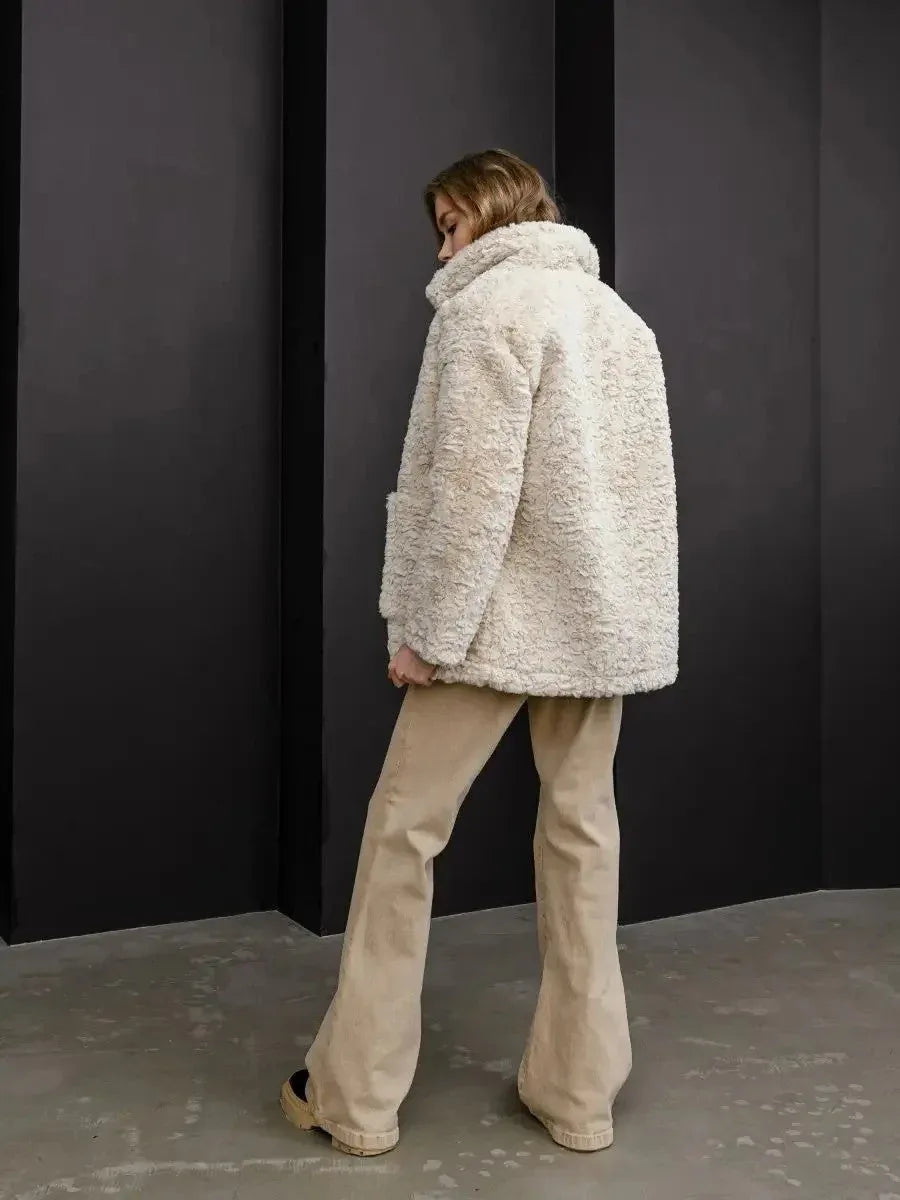 Rear view of the model wearing the cream faux fur coat and tan trousers.