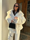 Woman smiling while wearing a white faux fur jacket with a relaxed fit and a black handbag.