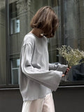 Side view of a woman in a light grey knit sweater with wide sleeves