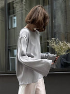 Side view of a woman in a light grey knit sweater with wide sleeves