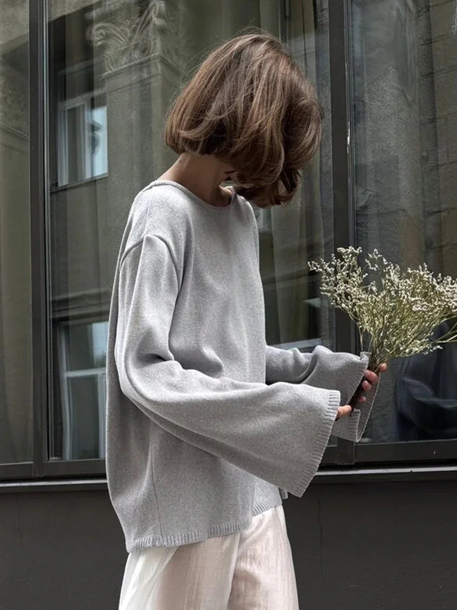 Side view of a woman in a light grey knit sweater with wide sleeves