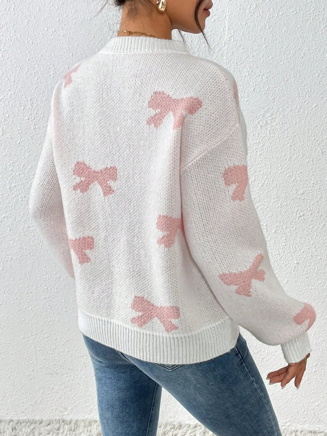 Woman wearing a white knit sweater with a pink bow print and crew neckline.