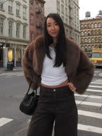Woman wearing a brown faux fur jacket and dark pants standing at a crosswalk