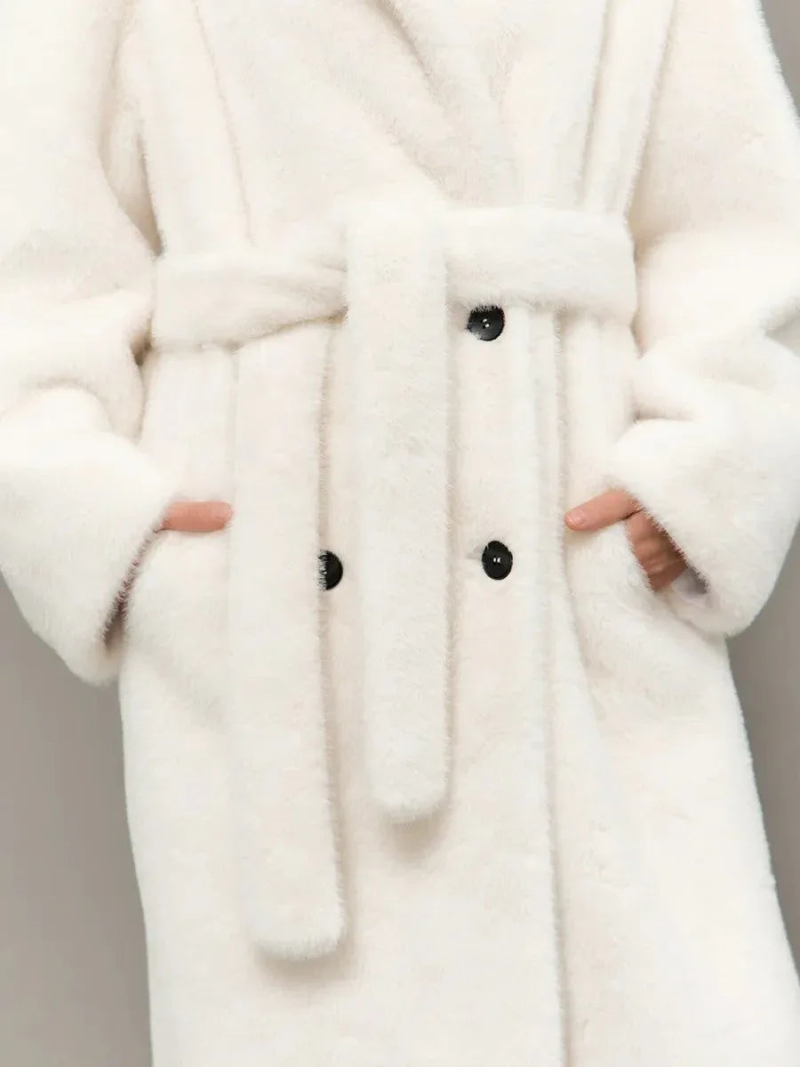 Full body shot of a woman in a long white hooded faux fur coat, holding a white handbag.