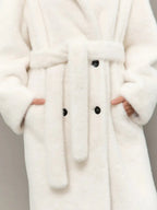Full body shot of a woman in a long white hooded faux fur coat, holding a white handbag.