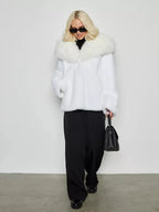 Woman wearing a white faux fur coat with black pants and a black handbag.