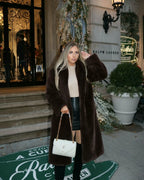 Woman wearing a long brown faux fur coat and a cream turtleneck