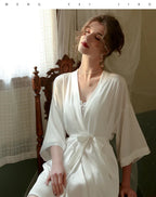 Woman posing in a full-length cream satin nightgown and robe set.
