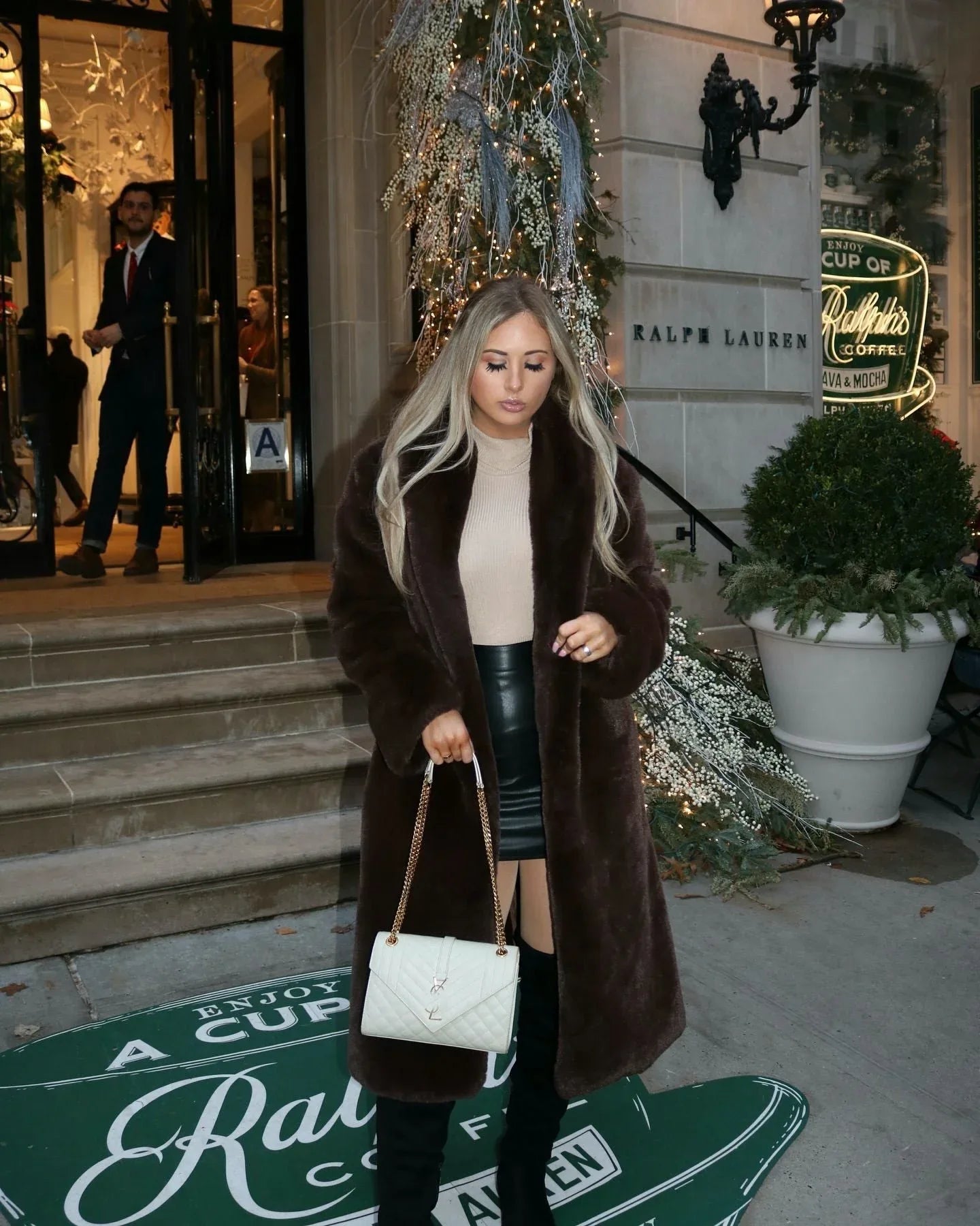 Woman in a long brown faux fur coat holding a white quilted handbag
